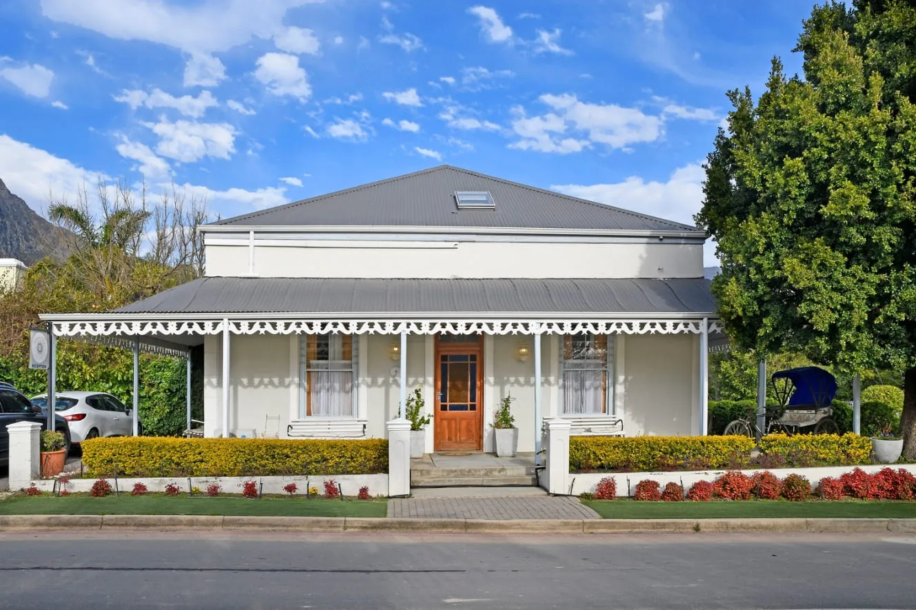 A quaint white house with a grey roof and vibrant garden under a blue sky