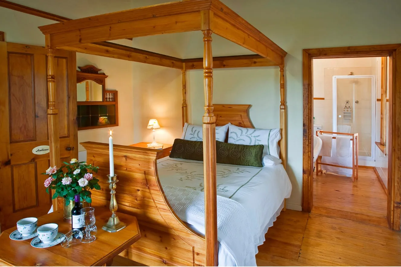 Wooden fourposter bed in a cozy bedroom with an open bathroom door