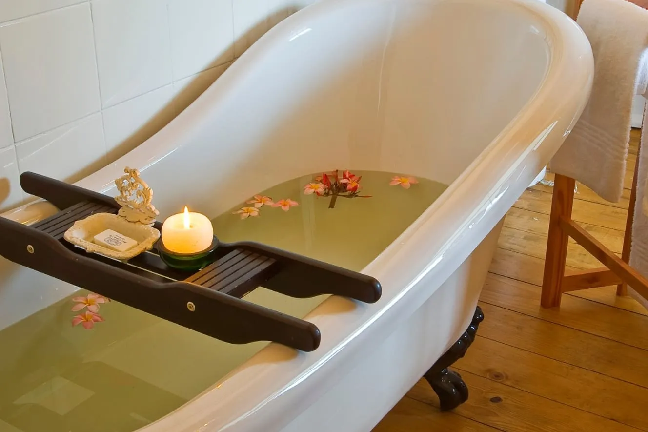 A bathtub filled with green water flowers and a lit candle on a tray