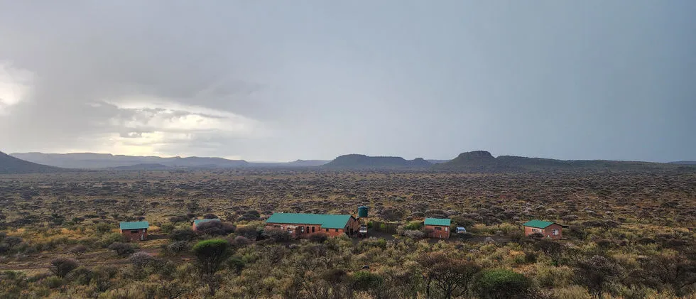 Small buildings in a vast open landscape with distant mountains under a cloudy sky