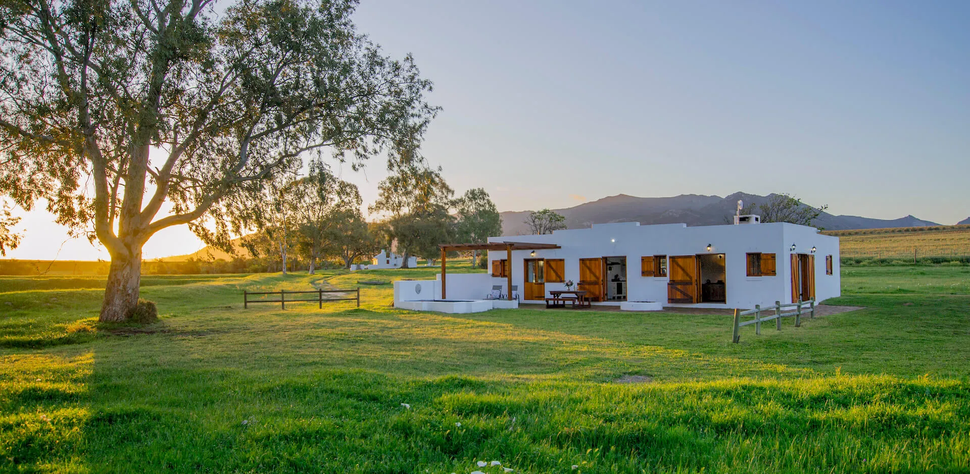 Modern house in a grassy field with trees and mountains in the background