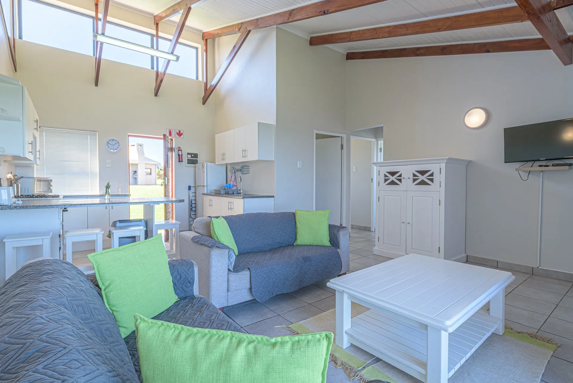 Cozy living room with grey sofas green cushions white coffee table and kitchen