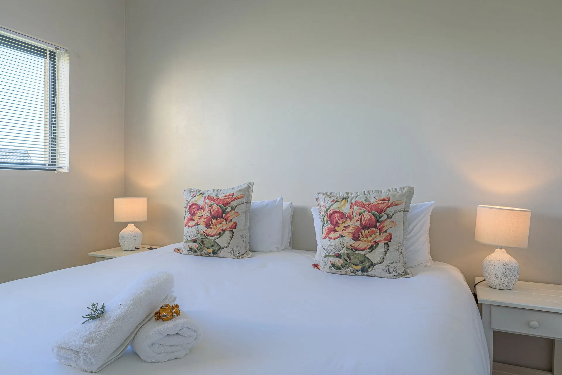 White bed with floral pillows towels and bedside lamps in a bedroom