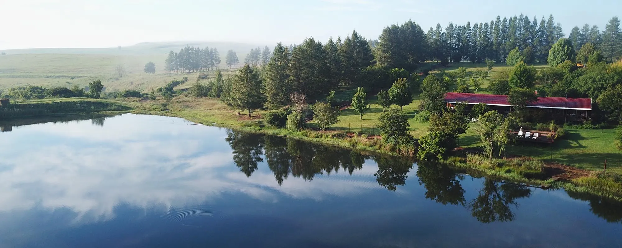 Aerial view of a serene lake with trees and a building with a red roof