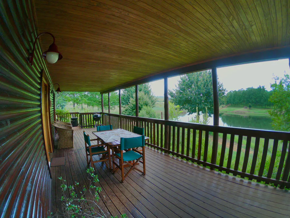 Wooden deck with table and chairs overlooking a lake surrounded by greenery