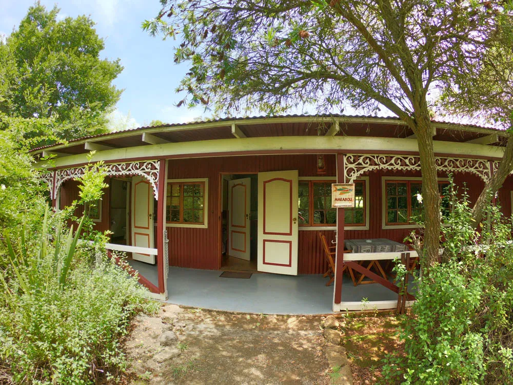 Wooden cabin with red doors and white trim surrounded by greenery