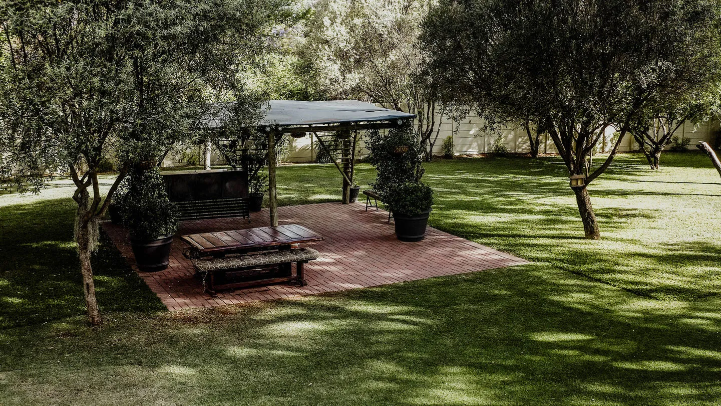 Wooden picnic table on brick patio surrounded by trees in a grassy area