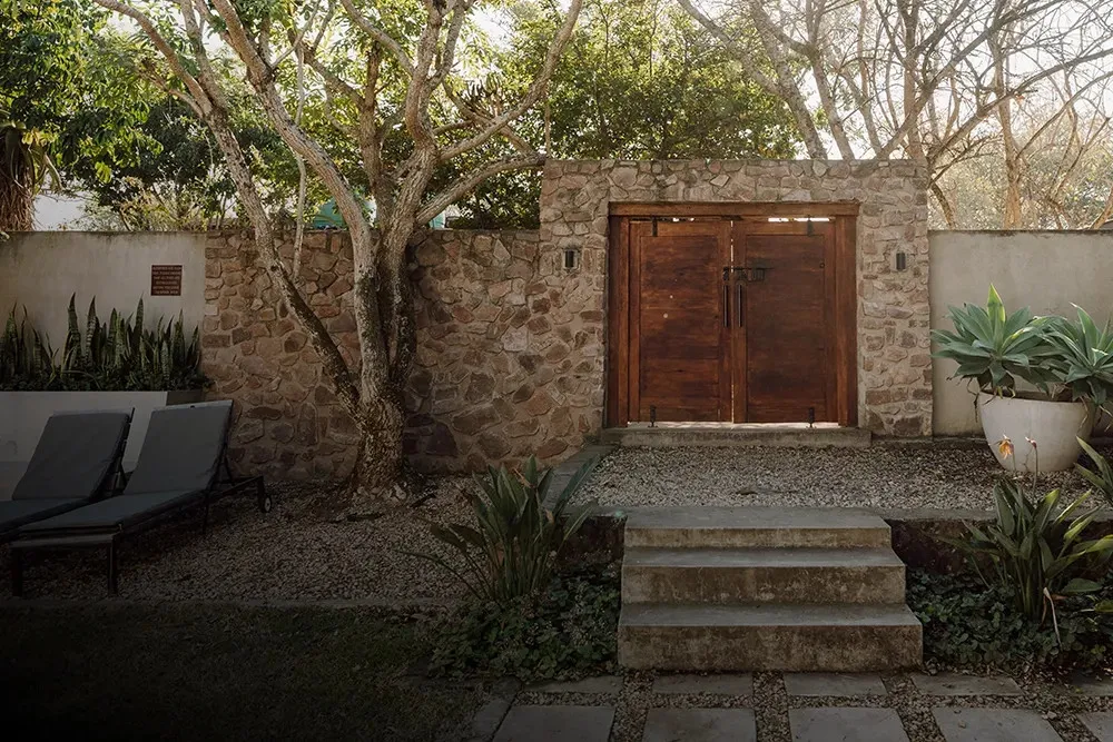 Wooden gate in stone wall with plants chairs and tree in a garden