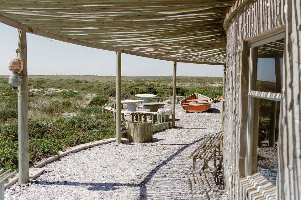 Wooden structure with seating and a boat in a coastal natural setting