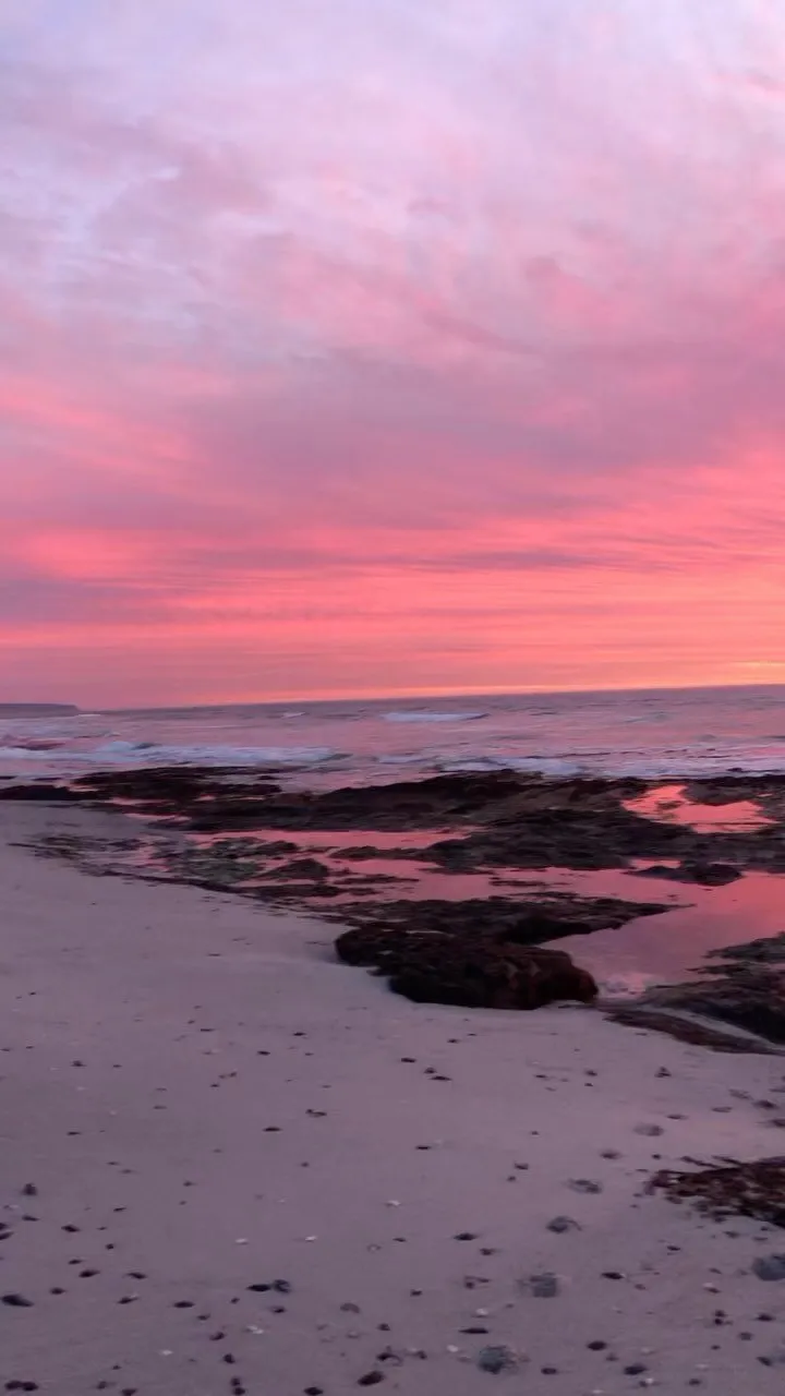 Beach at sunset with pink sky waves and rocky shore