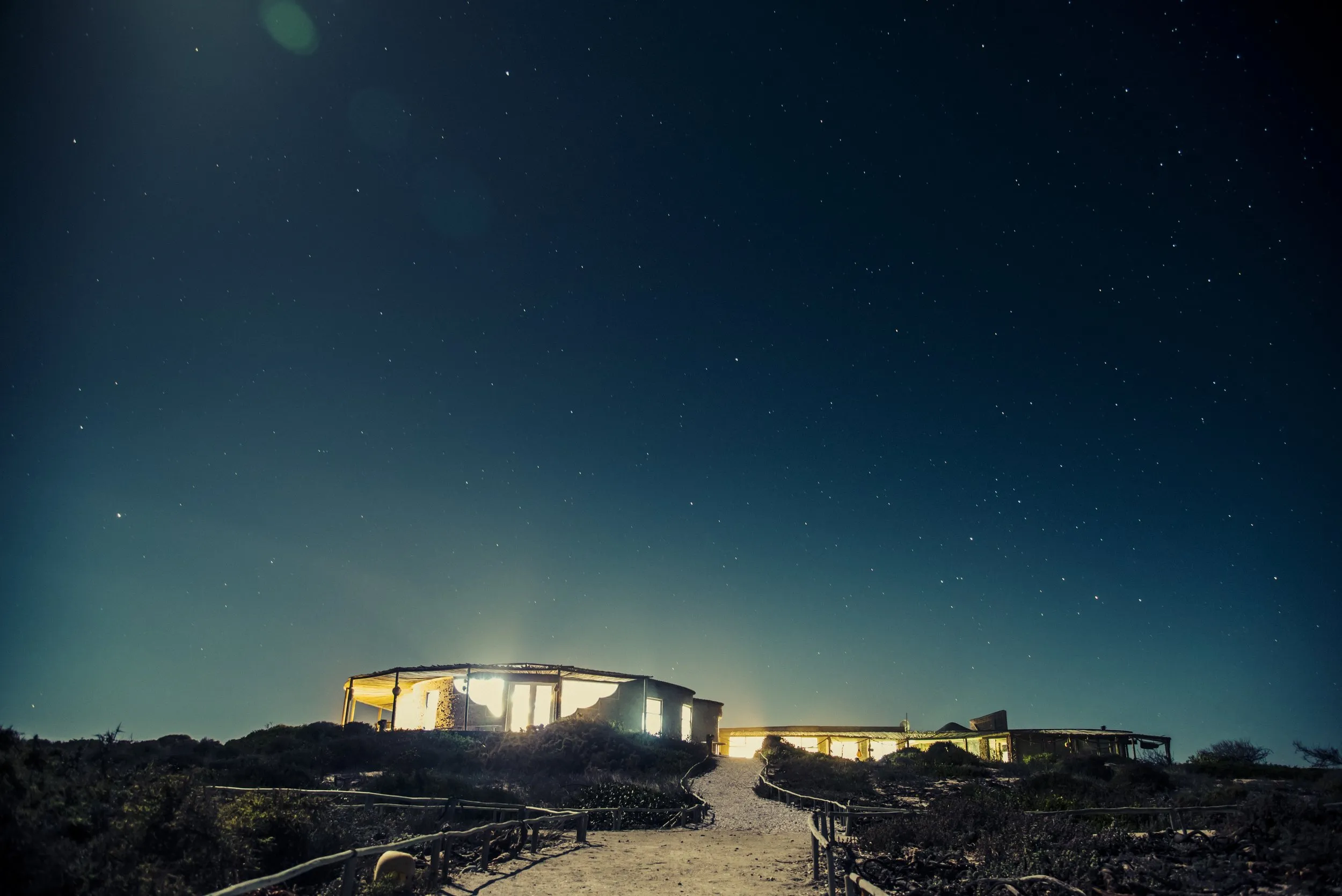 Modern house illuminated at night under a starry sky with a pathway leading to it