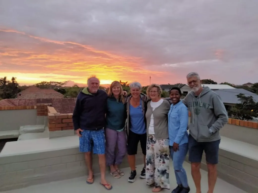 Group of six friends posing on a rooftop at sunset
