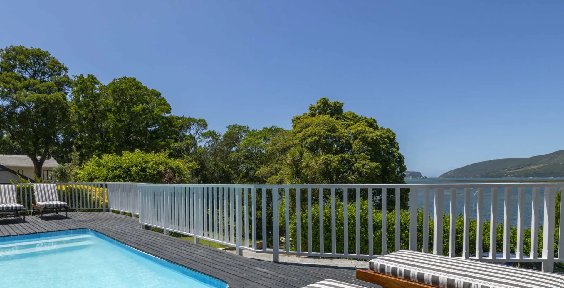 Swimming pool with deck chairs white railing and scenic view of greenery and hills