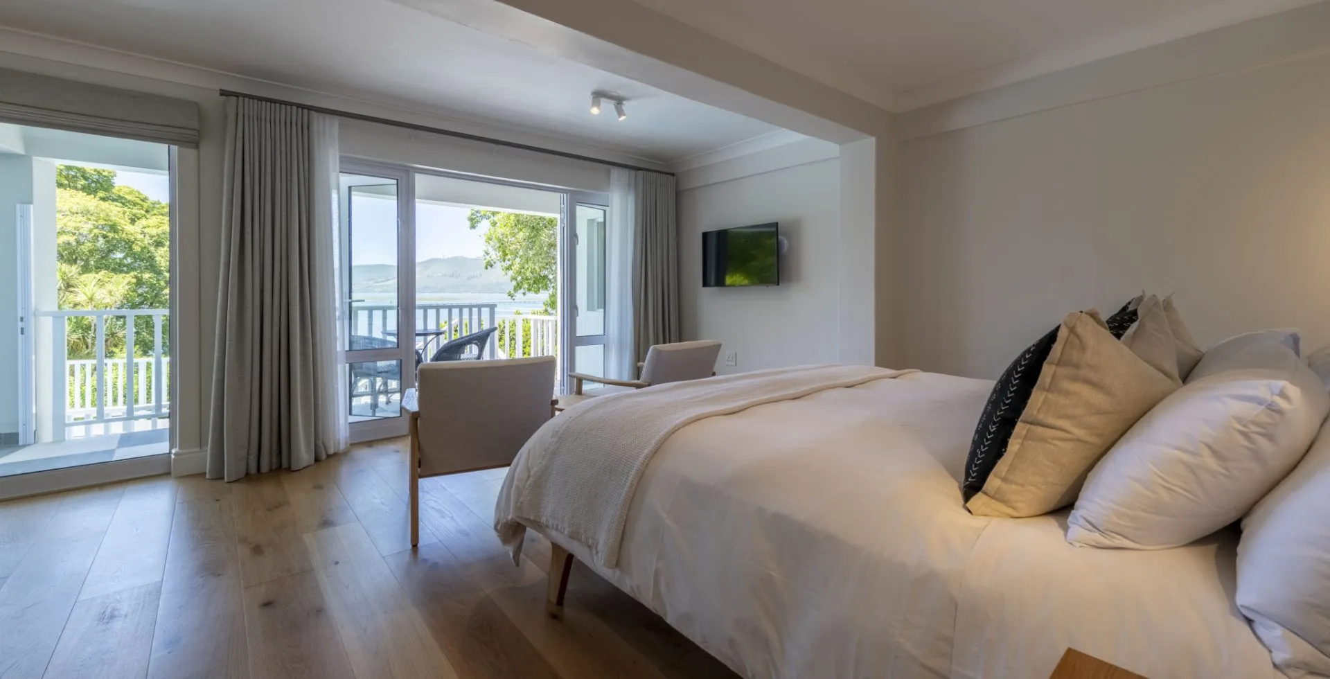 Bedroom with large bed pillows and a view of a balcony and greenery