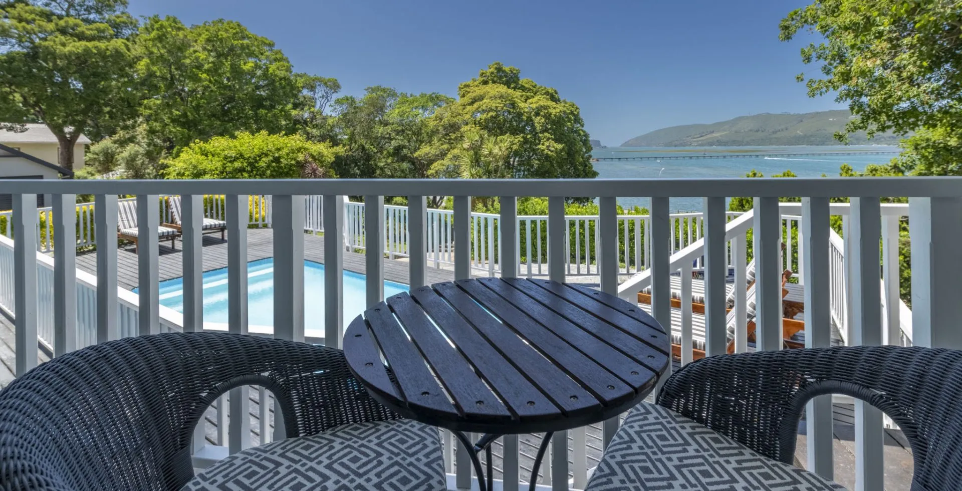 Two chairs and a table on a balcony overlooking a pool and lake