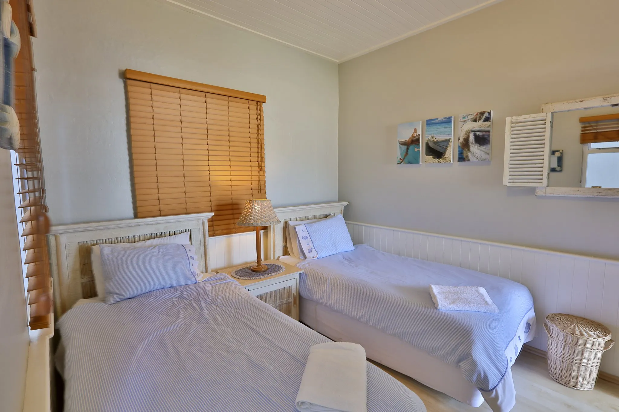 Two single beds in a tidy bedroom with wooden blinds and nautical artwork
