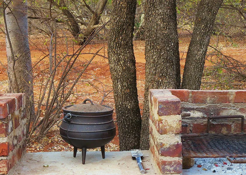 A black pot on a stand near a brick barbecue and trees