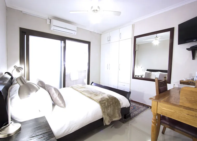 Modern bedroom with large bed sliding door wardrobe mirror and desk with TV