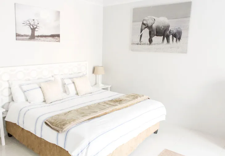 White bedroom with striped bed elephant artwork and tree photo on walls