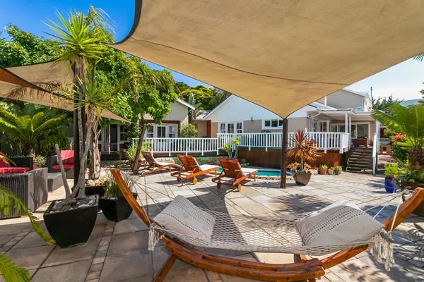 Wooden hammock in a sunny backyard with plants and a house in the background