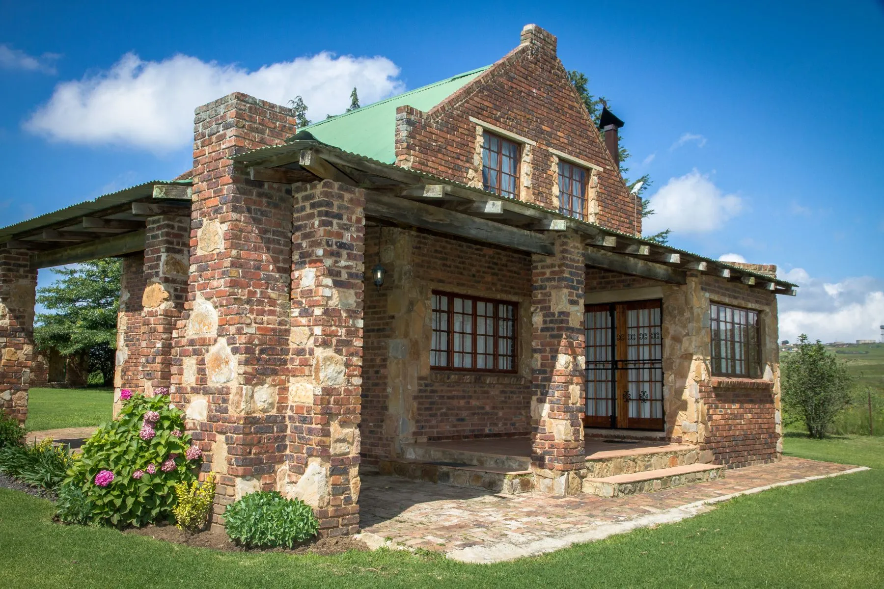 Brick house with green roof and stone pillars in a grassy area