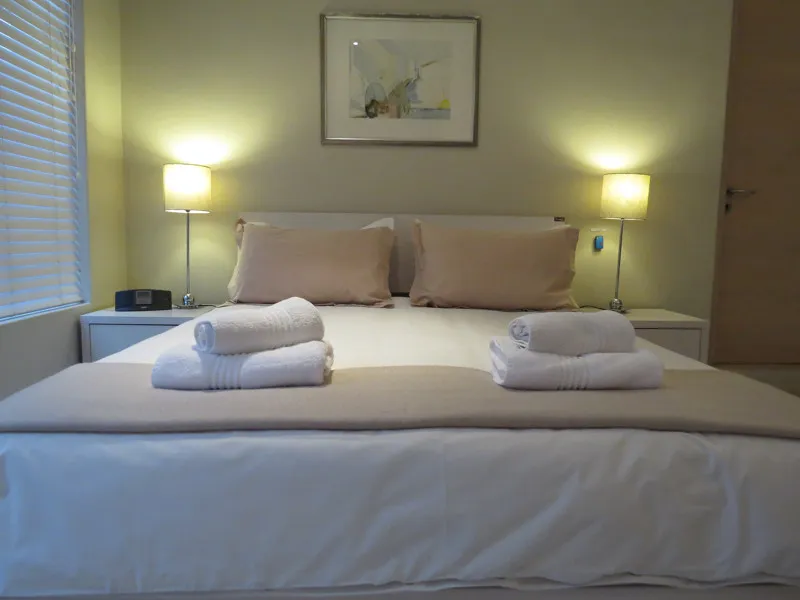 Neatly made bed with folded towels two lamps and a framed picture above