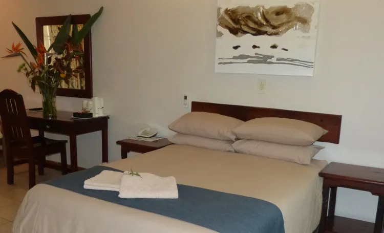 Neatly made bed in a simple hotel room with a desk and mirror
