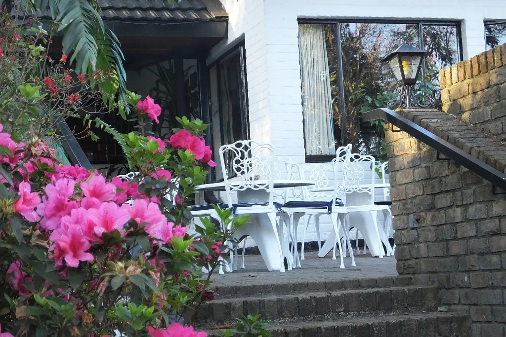 White patio furniture on a brick terrace with vibrant pink flowers in the foreground