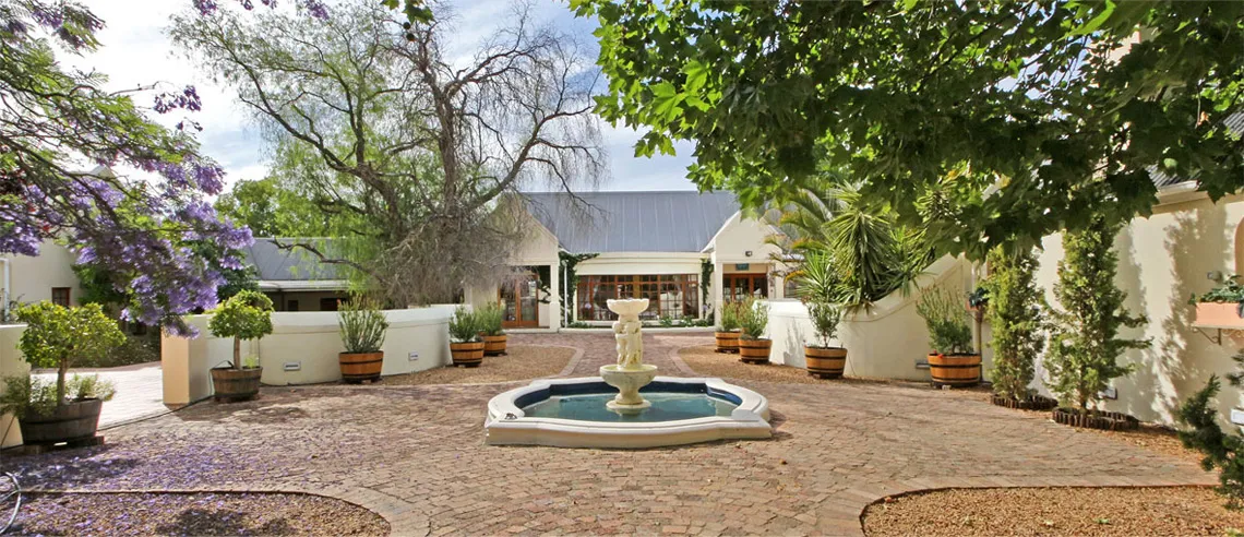 Courtyard with fountain potted plants and trees in front of a building