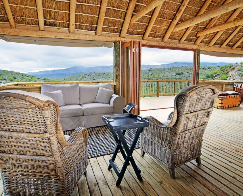 Wicker chairs and sofa on a wooden deck with scenic mountain view
