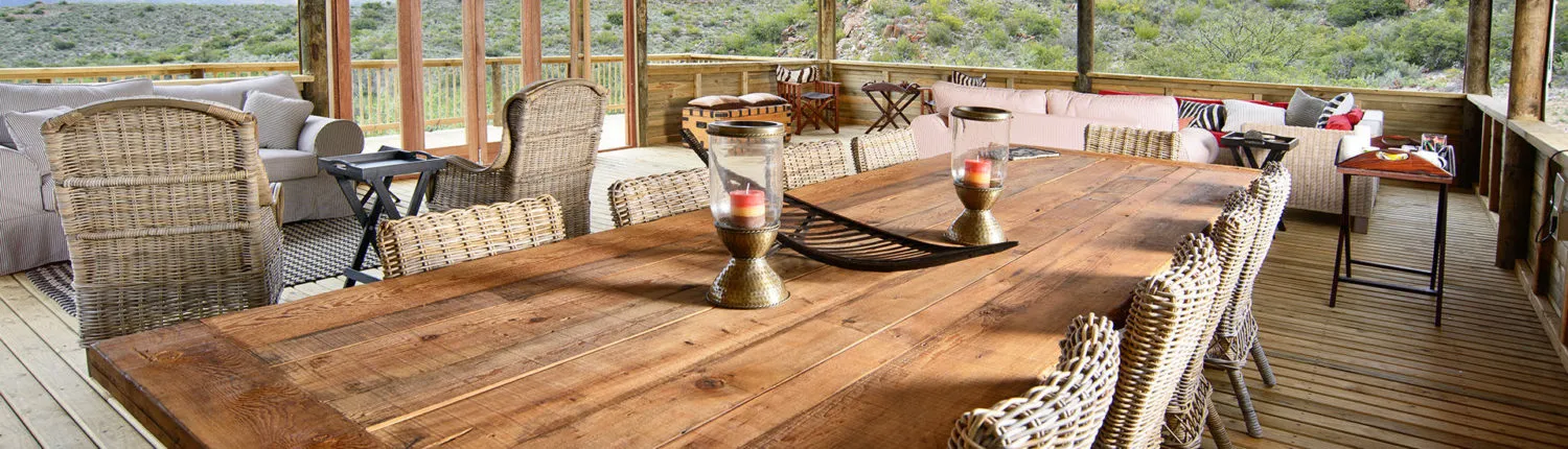 Wooden dining table with wicker chairs on a covered outdoor patio with scenic view