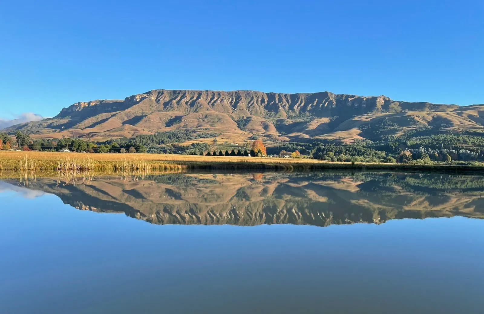 Mountain range reflected in a calm lake under a clear blue sky