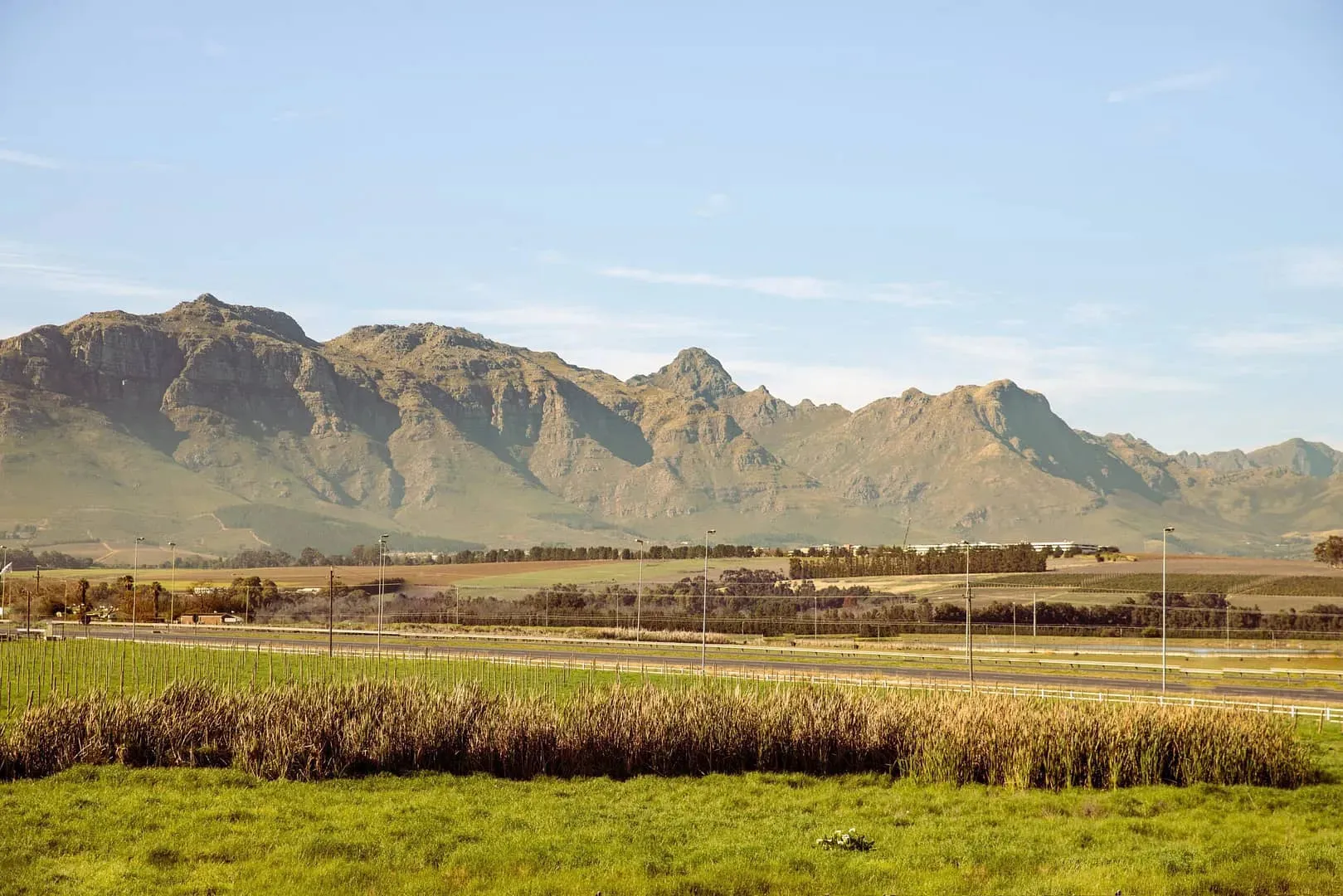 Mountain range with fields and road in the foreground under a clear sky