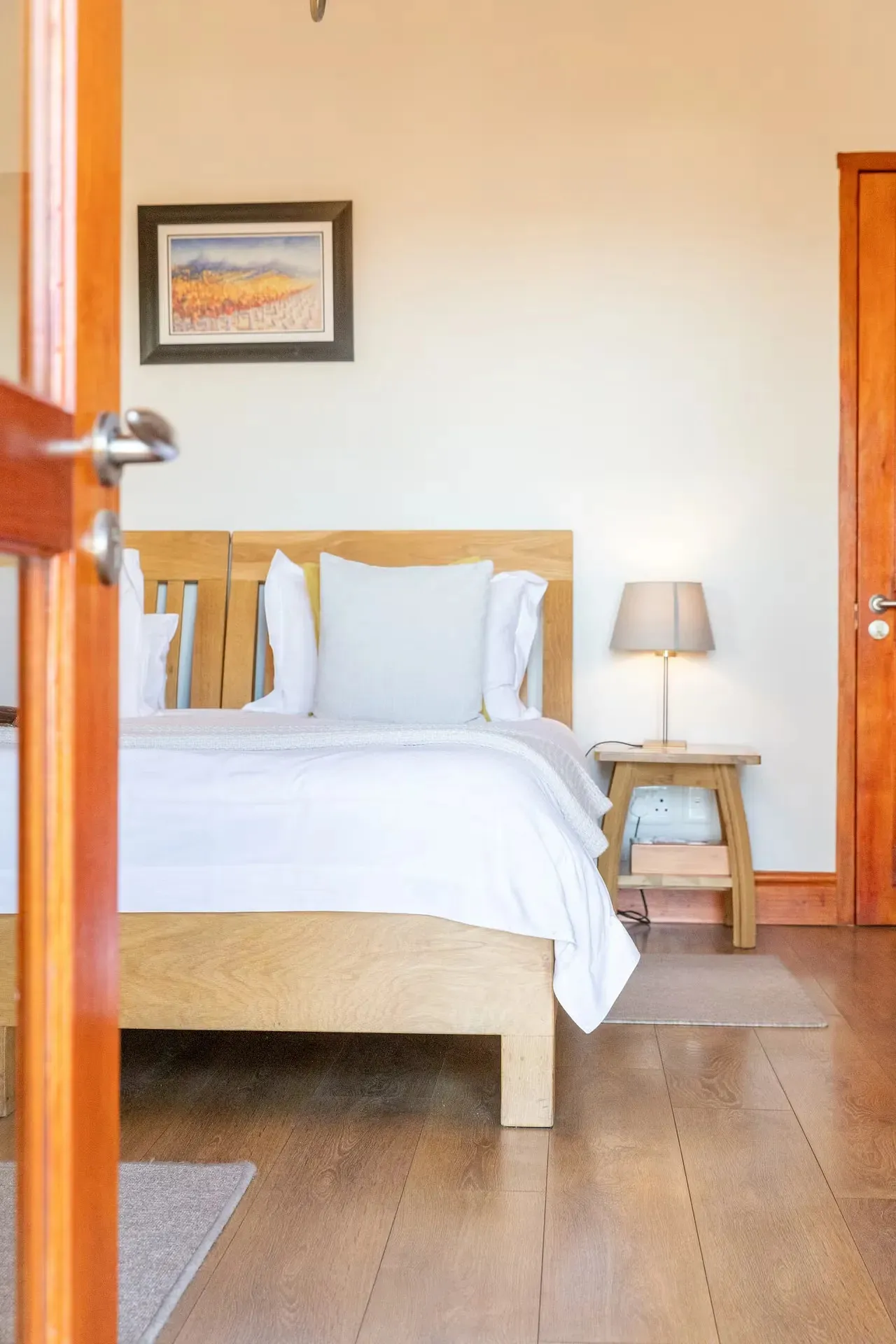 Bedroom with wooden bed white bedding bedside lamp and wooden floor