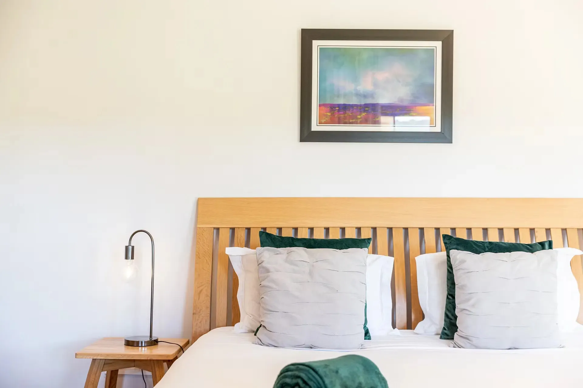 Wooden bed with white pillows green cushions and a bedside lamp in a bedroom