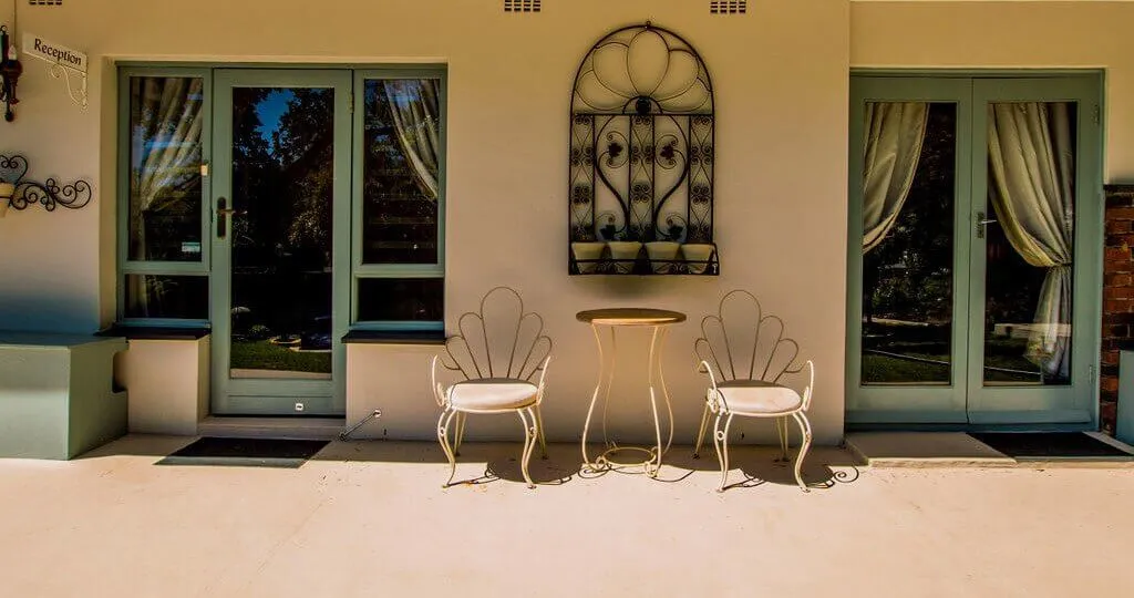 Two chairs and a table on a patio with green doors and windows