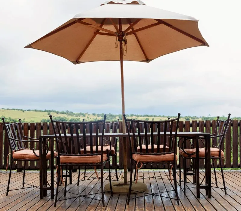 Wooden chairs with cushions under a large umbrella on a wooden deck
