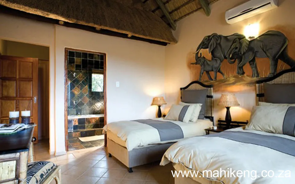 Cozy bedroom with two beds elephant decor and a stonetiled bathroom entrance