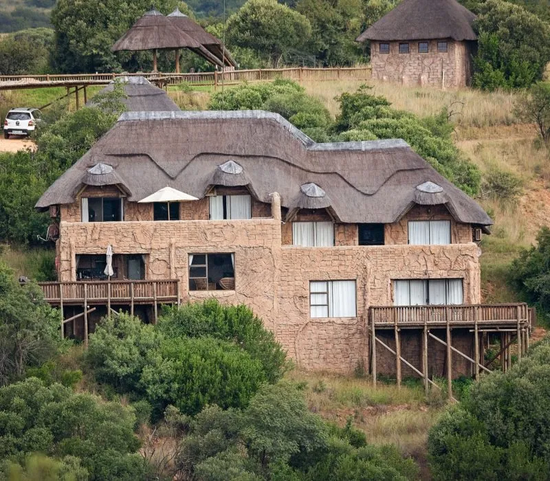 Large house with thatched roof on a hillside with trees and a deck
