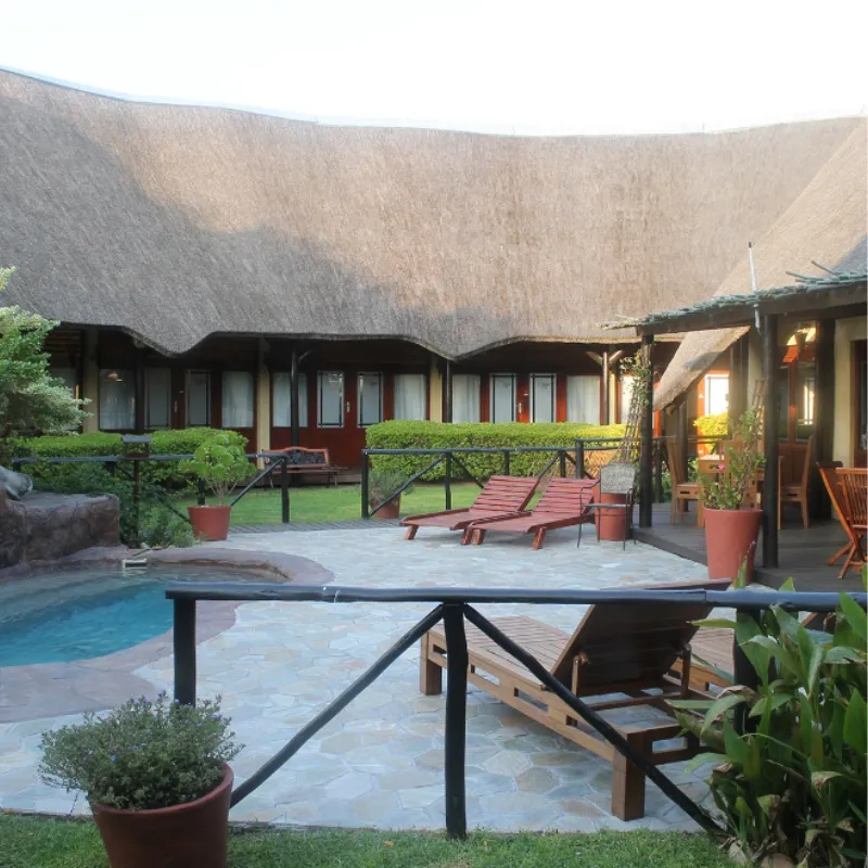 Thatchedroof building with lounge chairs plants and a small pool in courtyard