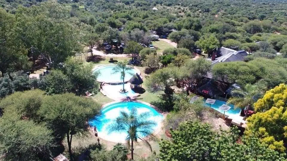 Aerial view of pools and huts surrounded by lush greenery in a resort