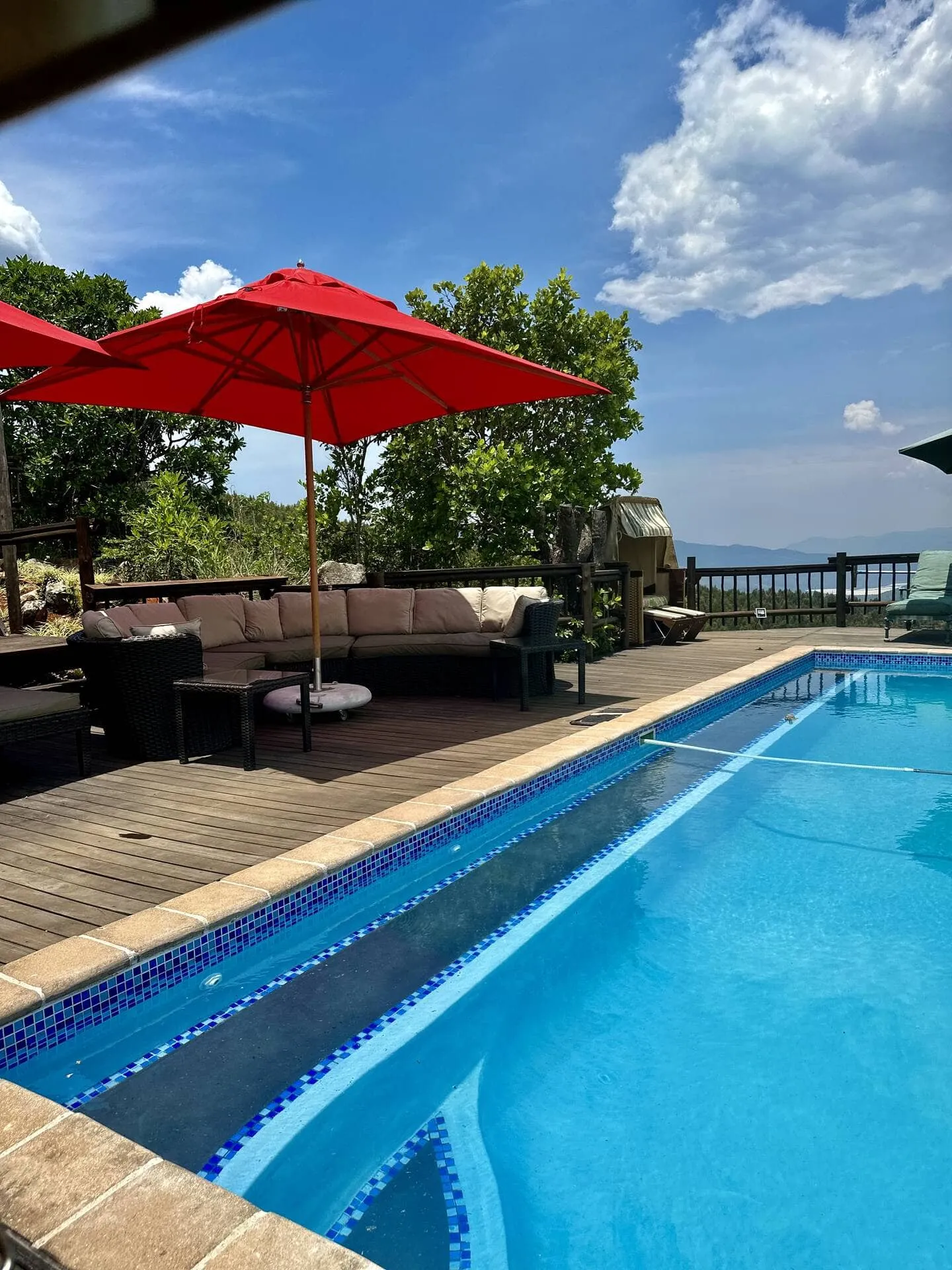 Wooden deck with pool lounge chairs and red umbrellas under blue sky