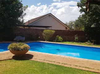 Swimming pool with potted plant in a backyard with a house in the background