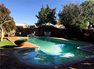 Swimming pool in a backyard with chairs trees and a brick wall