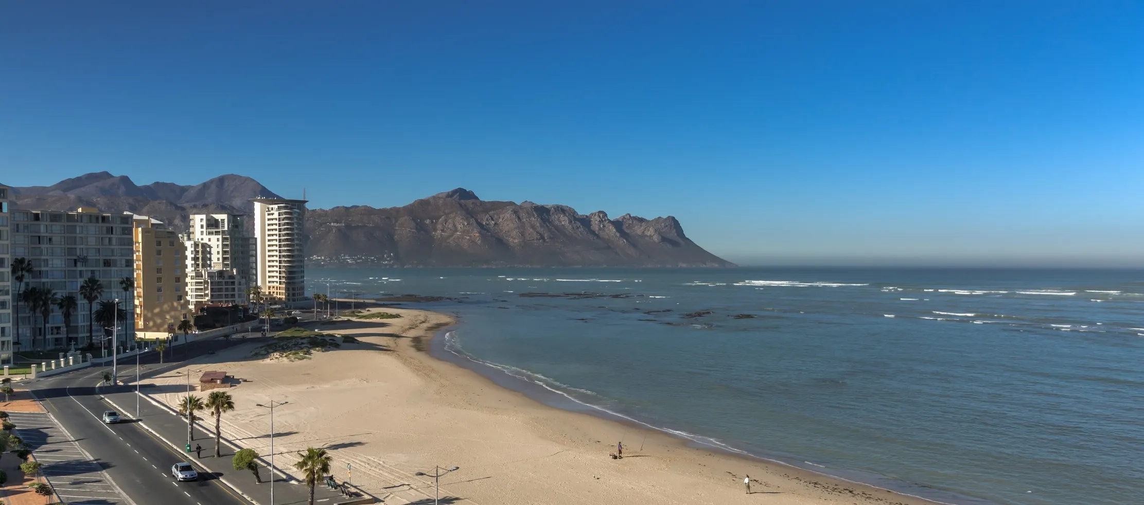 Beach with highrise buildings mountains in the background and a clear blue sky