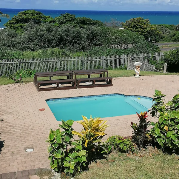 Swimming pool with wooden lounge chairs overlooking the ocean and greenery