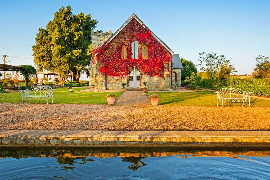Small stone chapel with red ivy garden benches and a reflecting pool