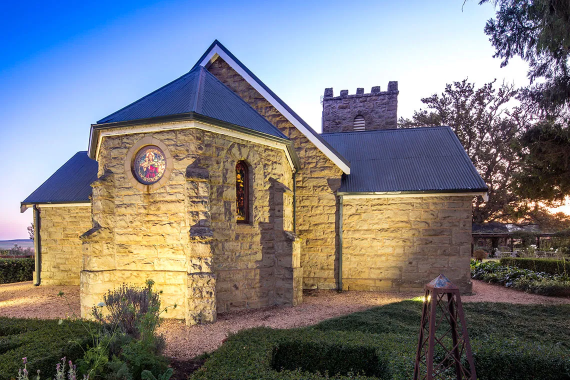 Stone church with stained glass window at dusk surrounded by greenery