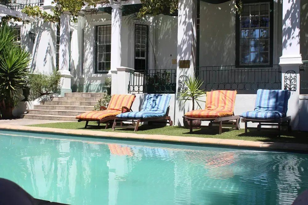 Four lounge chairs by a pool in front of a white building with columns