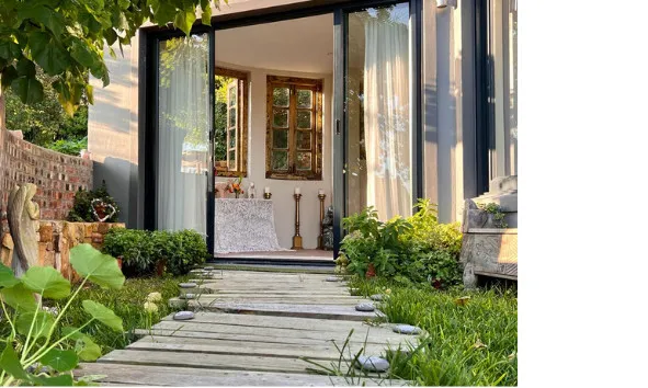 Wooden path leading to a cozy room with open glass doors and plants